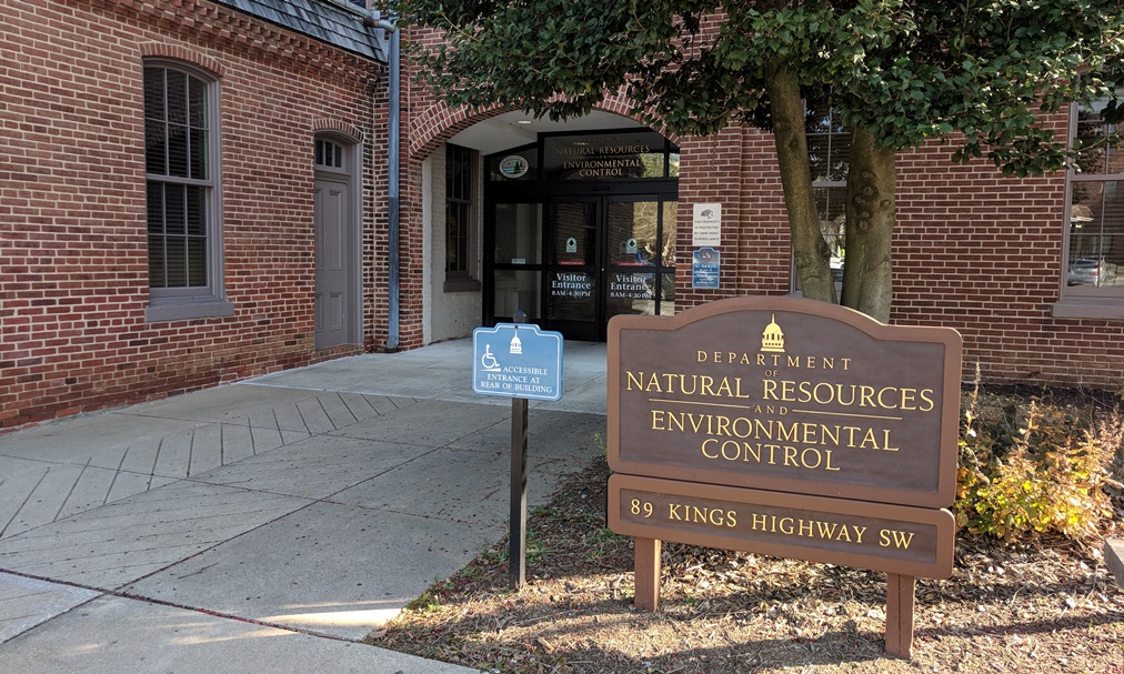 Entrance to a brick building with a sign reading "Department of Natural Resources and Environmental Control" and "89 Kings Highway SW."