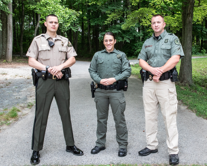 Three law enforcement officers, a woman standing between two men, pose in different uniforms of the Delaware Natural Resources Police.