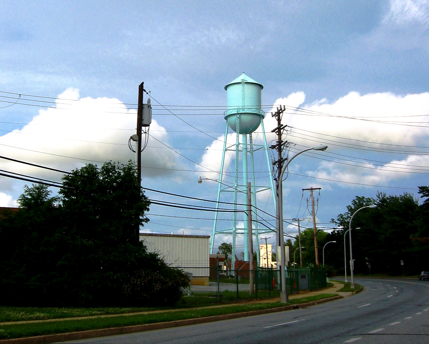 A view of an industrial water tank on a tower over a road that runs next to a warehouse.