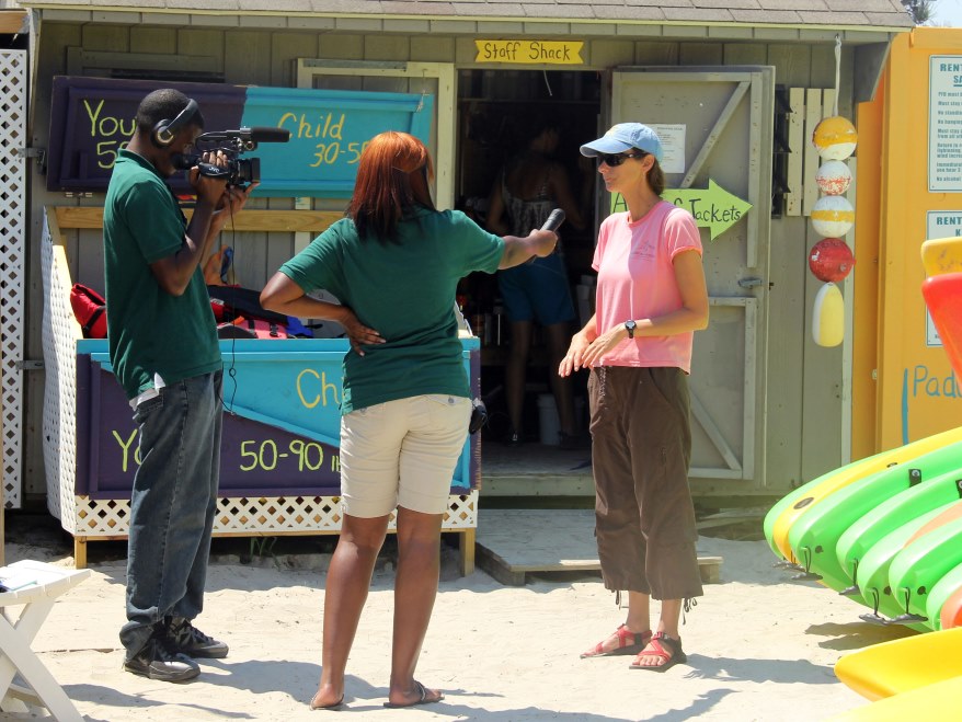 A pair of interns conduct an interview in front of a beach staff shack.