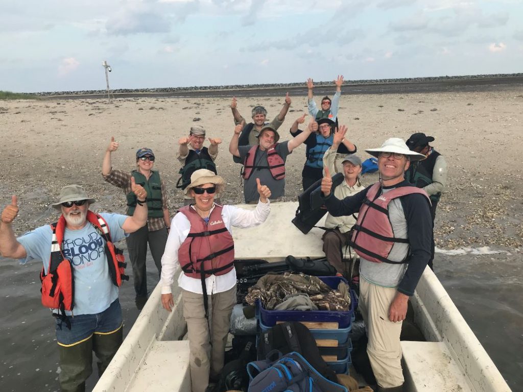 A group of smiling, waving volunteers pose on a beach.