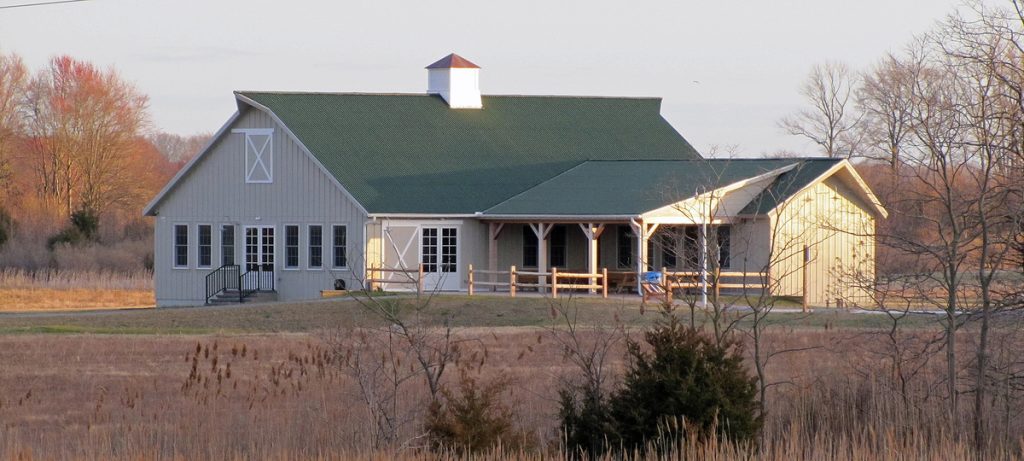 A barn-like building seen from across a field in fall. It has a covered porch and shed-style wing.