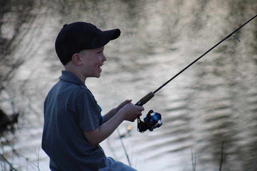 A happy child is seen fishing at a pond.