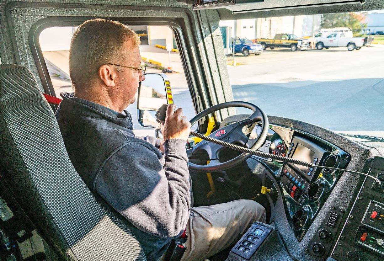 An emergency manager sits in the cab of a large truck, speaking into a radio micrphone.