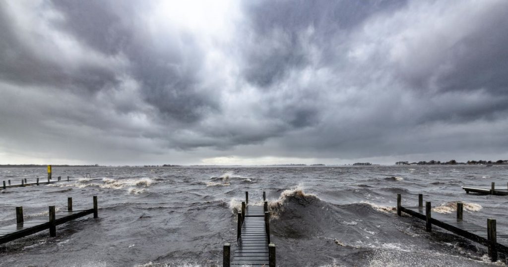 Storm-driven waves break over wooden docks extending into a salt-water bay.