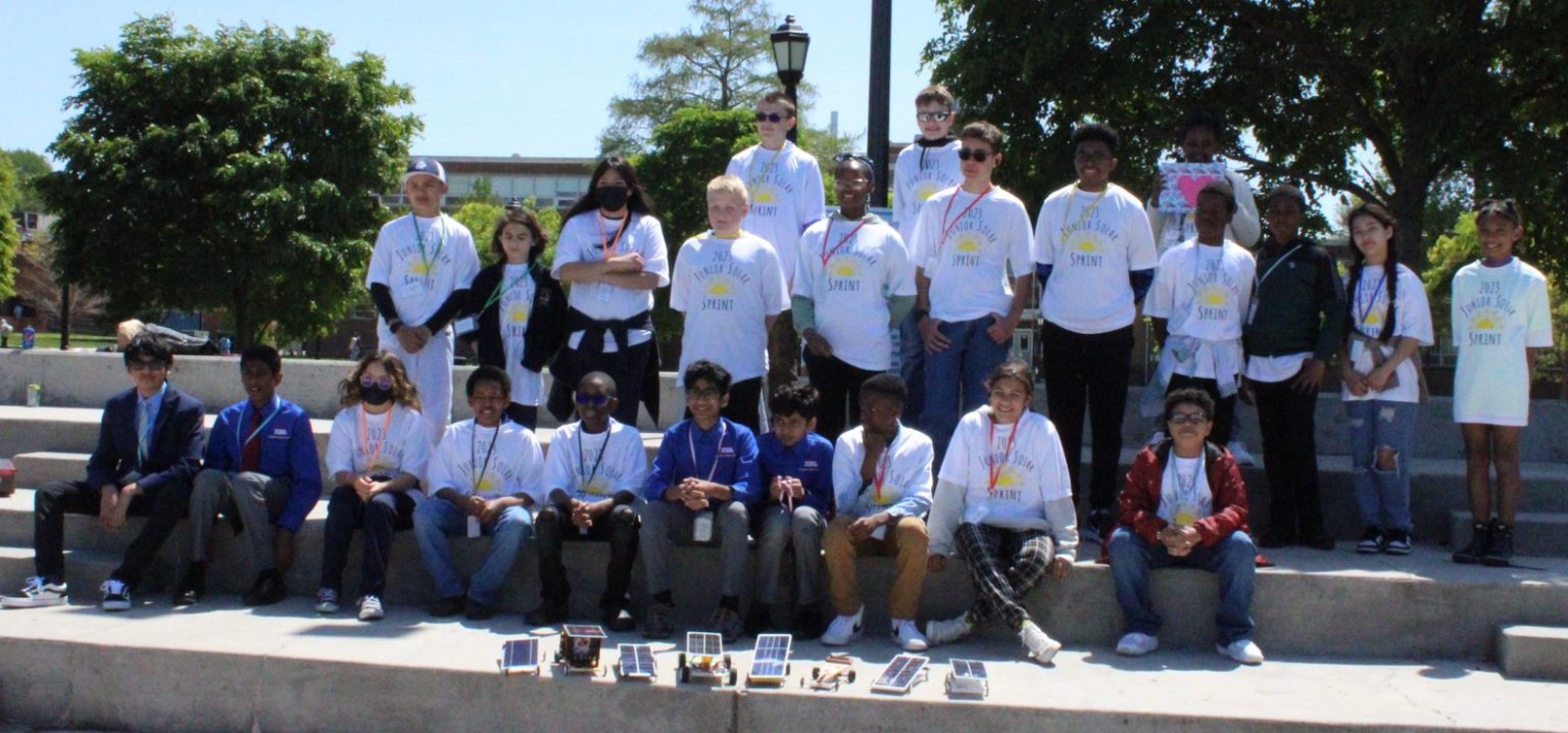 A large group of students pose with their solar-powered model vehicles.