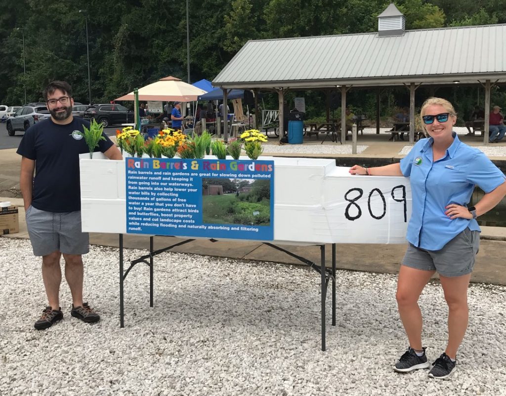 Two staff members pose outdoors with a display of planting ideas.