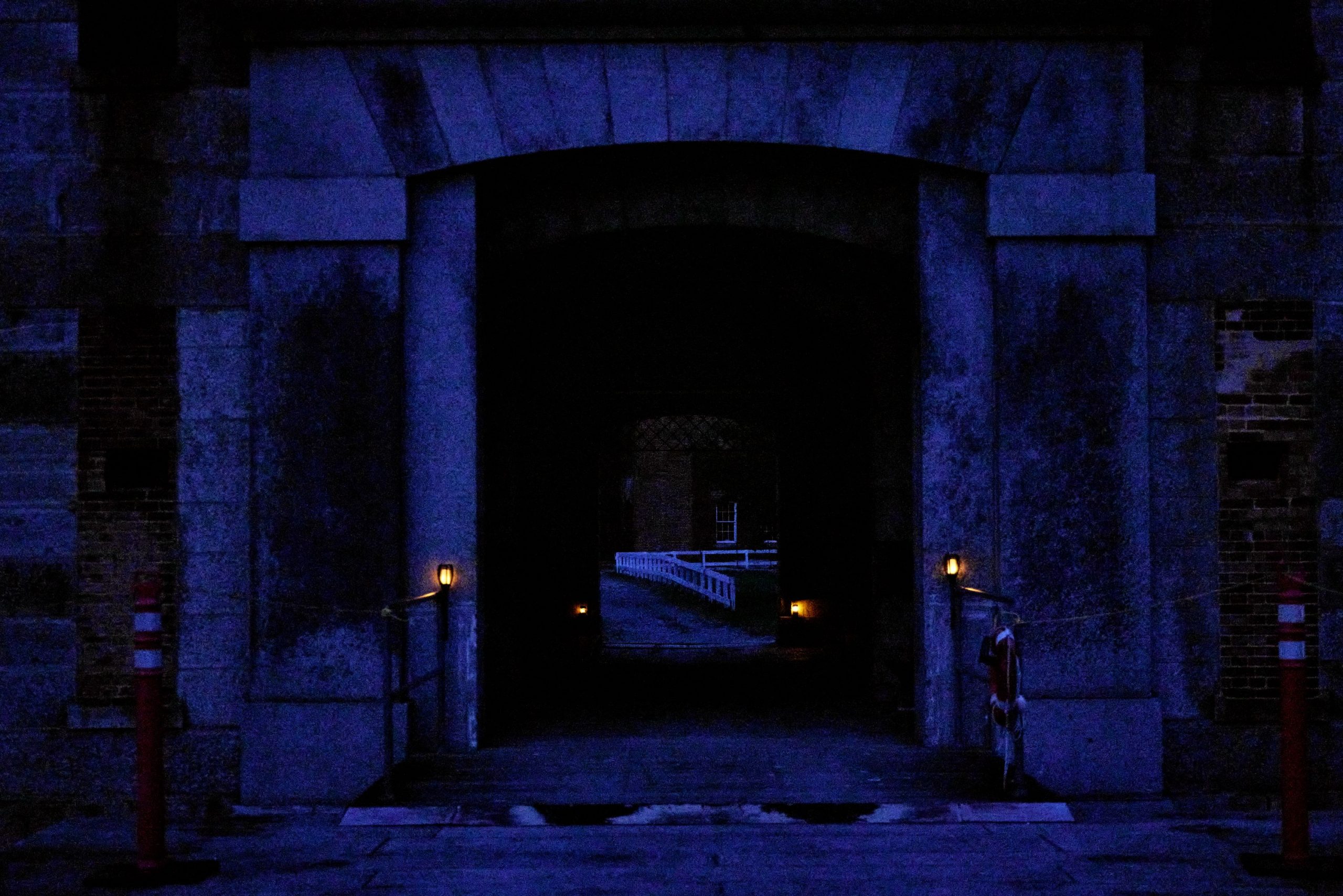 A night scene showing the entry gate of a masonry fort lit by old-fashioned lanterns.