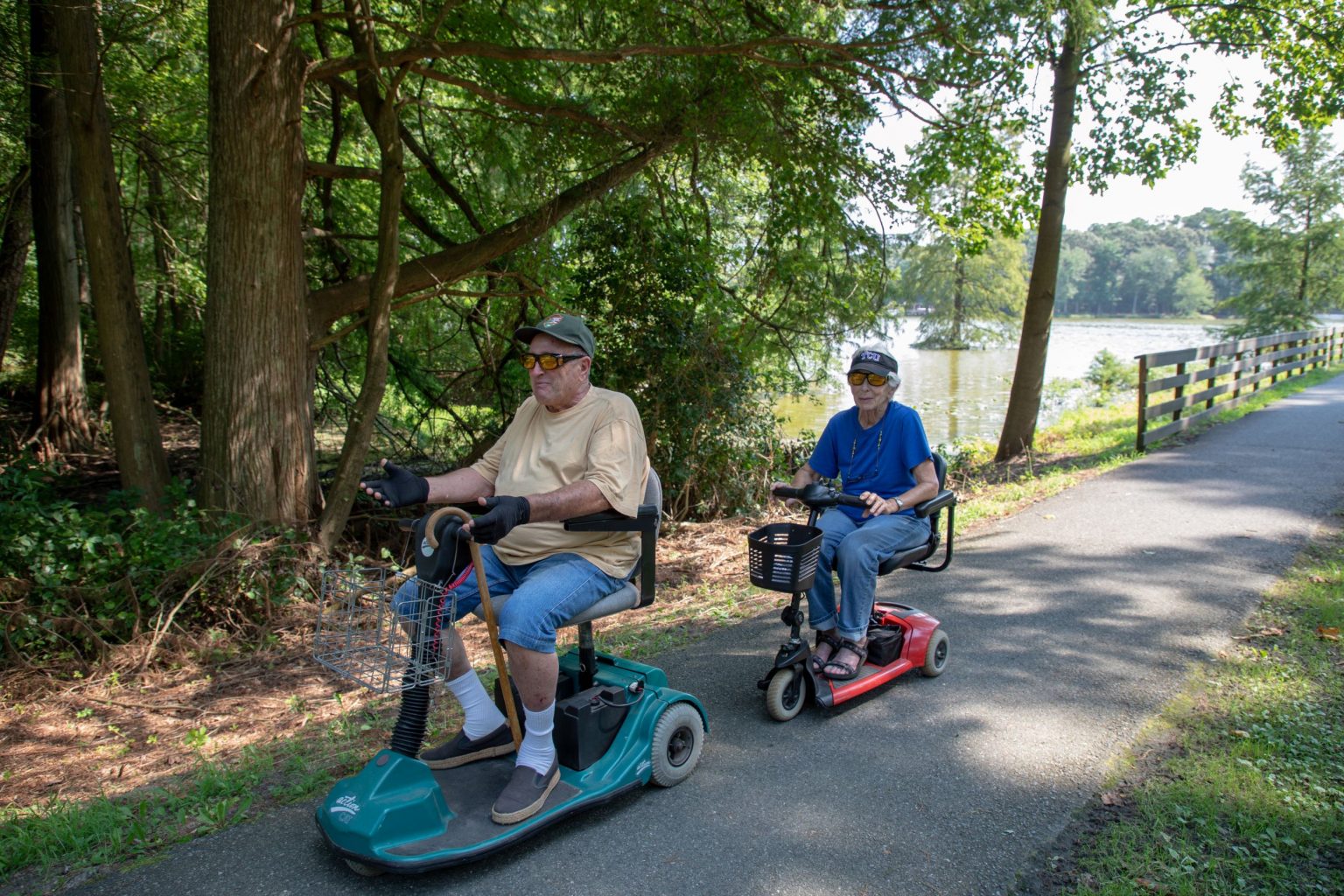A man and woman on accessibility scooters on a park trail