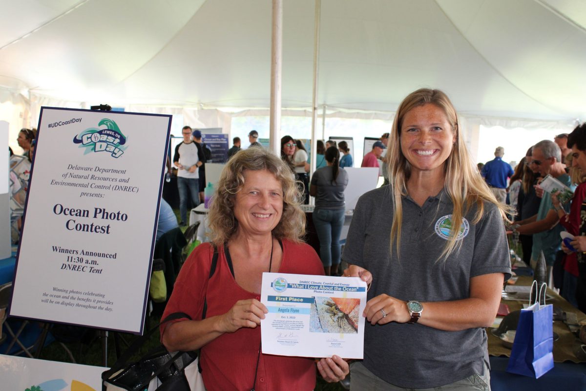 Two women in a tent pose together with a contest certificate.