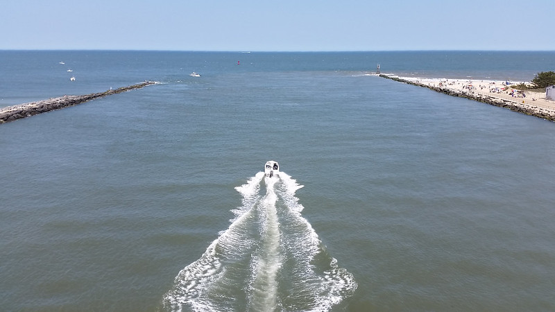 A small boat heads out to sea through an inlet defined by two stone jetties.