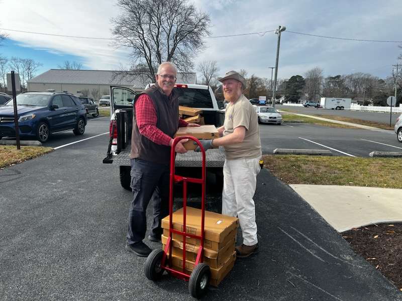 A DNREC staff person hands boxes of processed deer meet to a volunteer at a distribution hub.