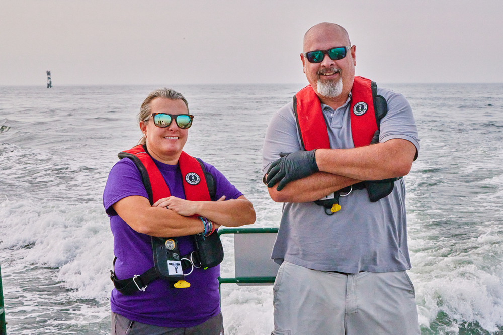 Two DNREC employees wearing personal flotation devices pose for a photo while on a boat on the Delaware Bay checking water quality.