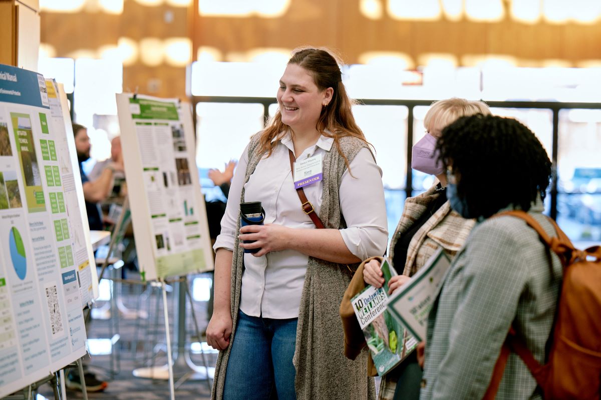 Three women stand together looking at posters displayed at a professional conference.