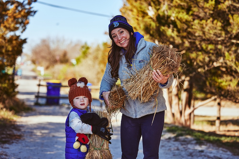 A young child and a woman pose for a photo outdoors. Each is holding a bale of beach grass to be planted.
