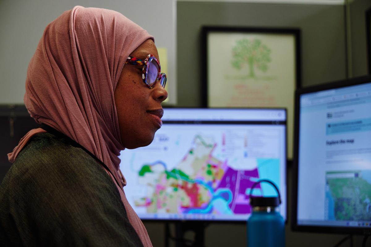 A woman examines data and map information on computer screens in an office.