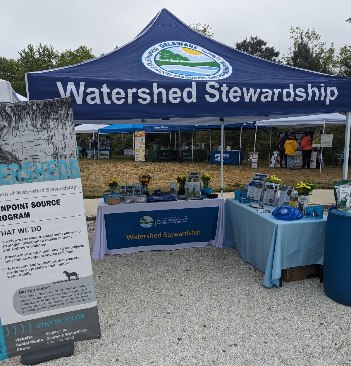 A blue tent, labelled "Watershed Stewardship" with two display tables and an information sign.