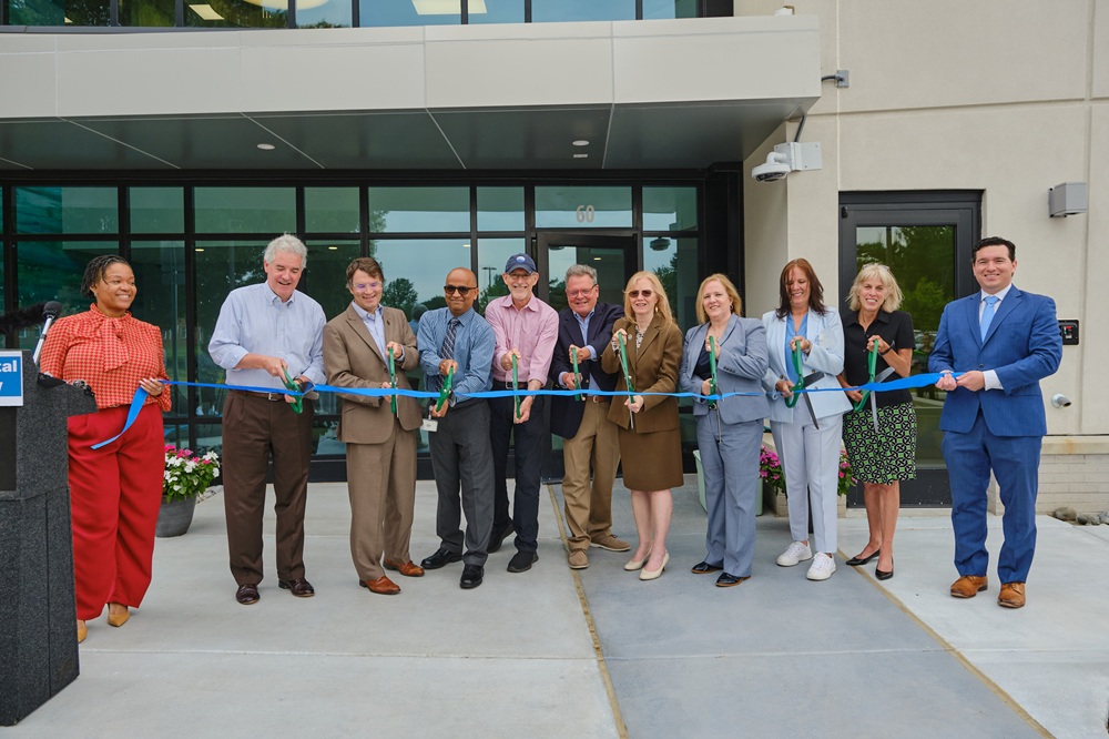 About a dozen people stand in front of a building holding giant ceremonial scissors for a ribbon-cutting.