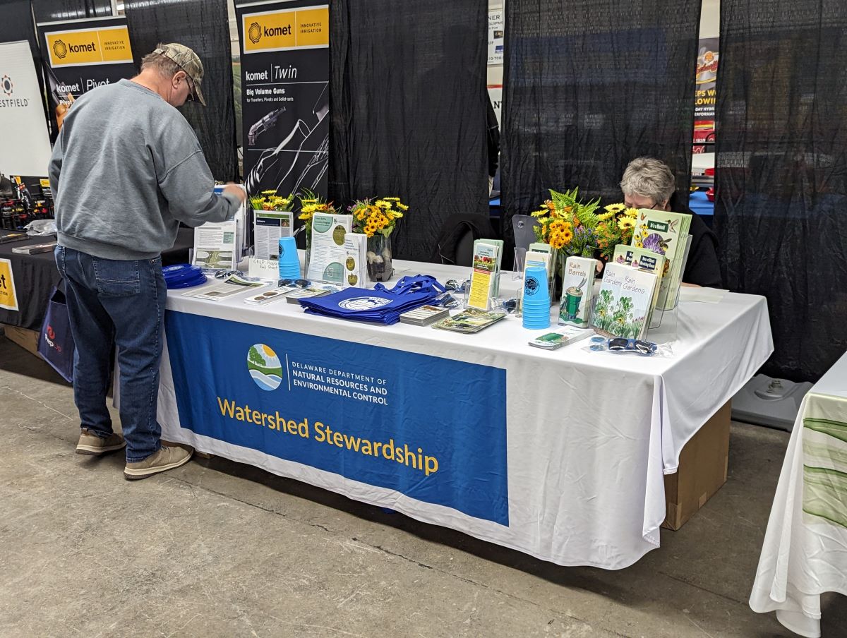 A man stands at a display table labeled "Watershed Stewardship" reading a brochure.