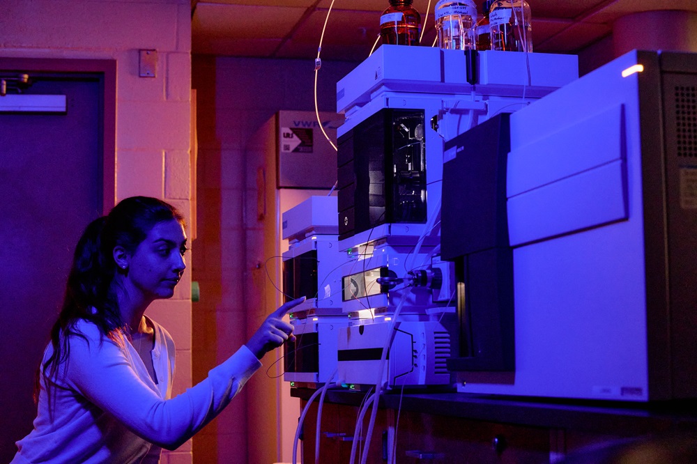 A woman touches a machine inside a laboratory in dim lighting.