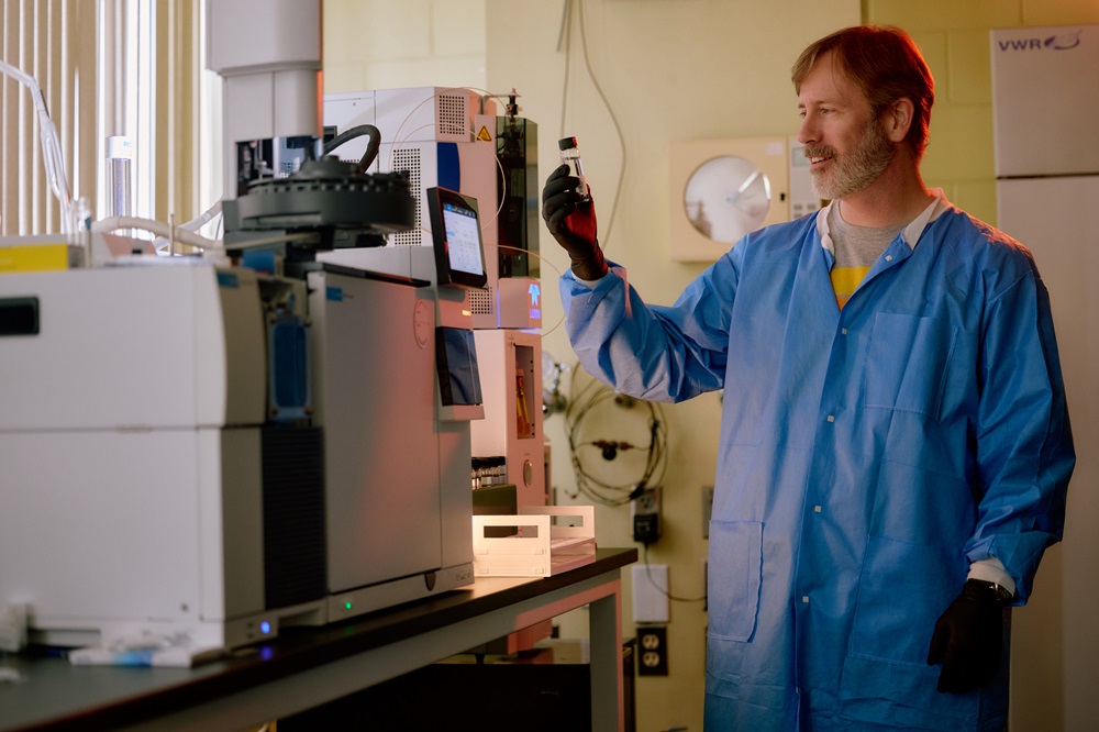 A man in a lab coat holds a vial of water.