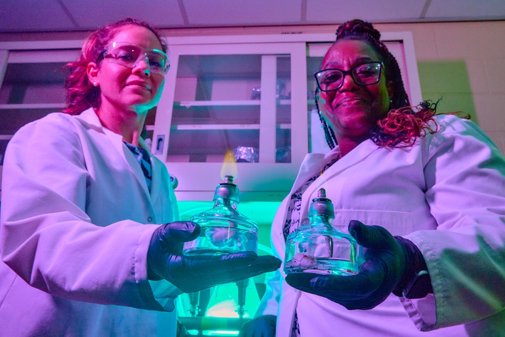 Two women in lab coats hold portable burners