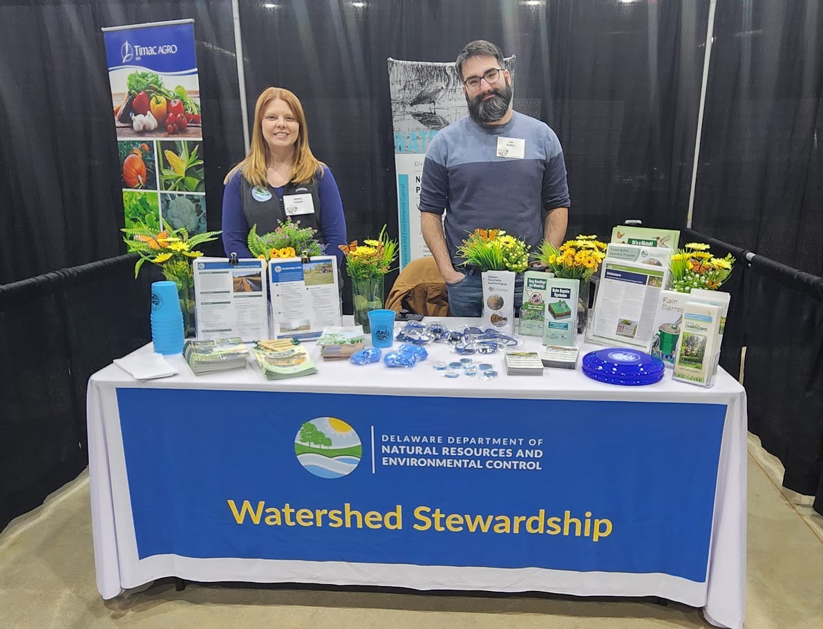 Two smiling people wearing name tags stand at a table with a "Watershed Stewardship" sign.