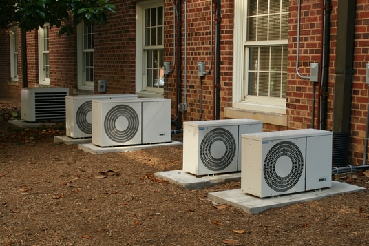 A line of heat pumps outside a brick building.