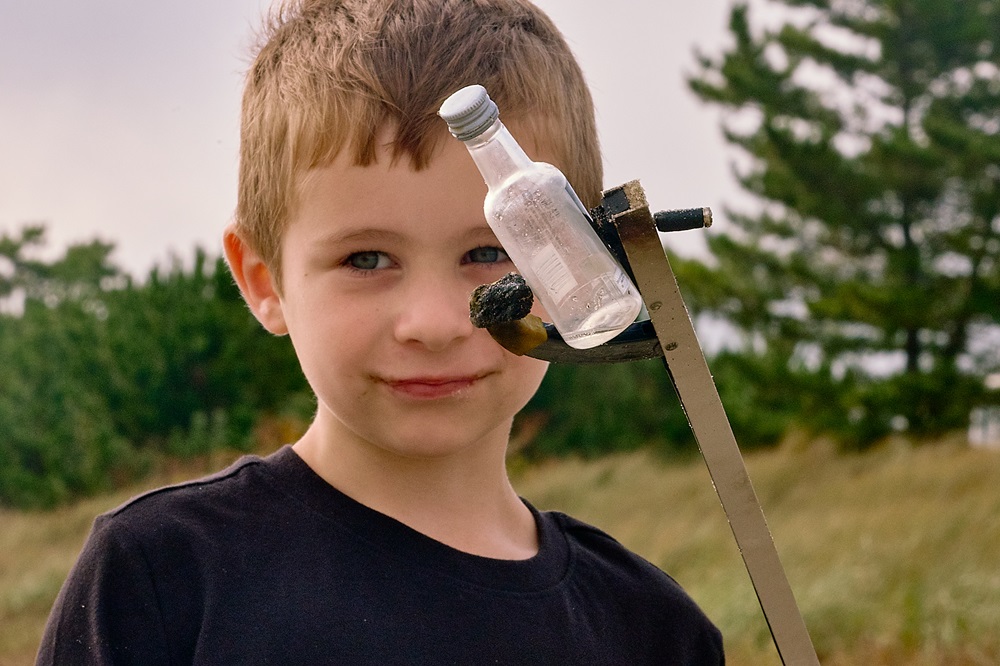 A boy holds an empty miniature bottle of alcohol in a mechanical grabber device.