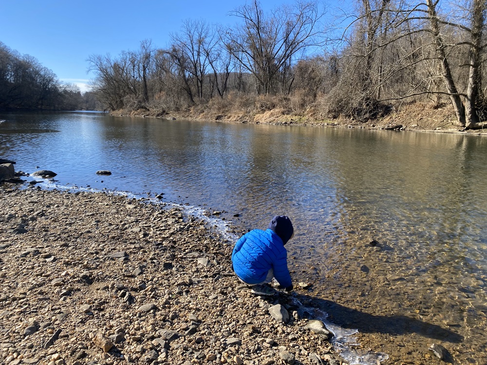 A young boy kneels down to touch the water in a creek.