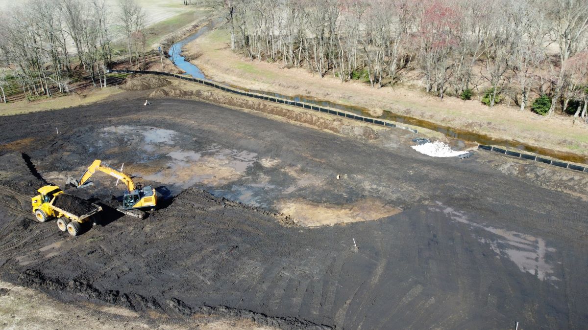 Aerial view of an excavator and a dump truck working to build a shallow water area.