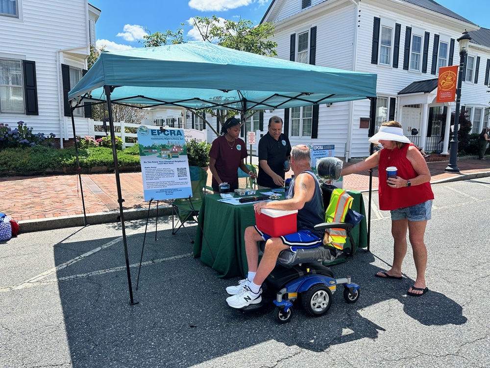 Several people, including a man in a wheelchair, visit a display about chemicals set up under a tent.