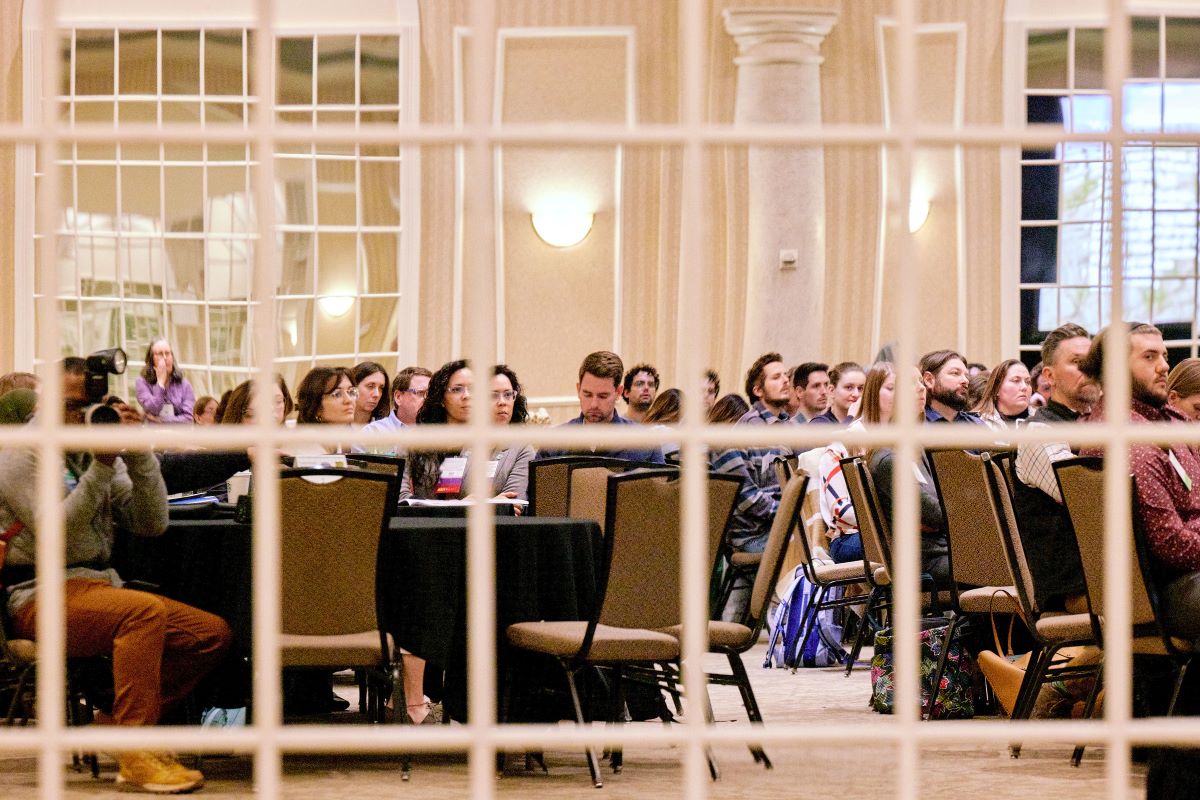 A group of attendees at a conference, seen in reflection of a many-paned window-style mirror.