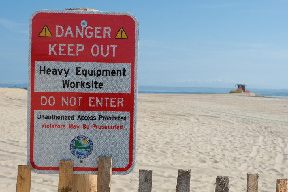 A sign warns beachgoers to stay out of a worksite with heavy machinery.