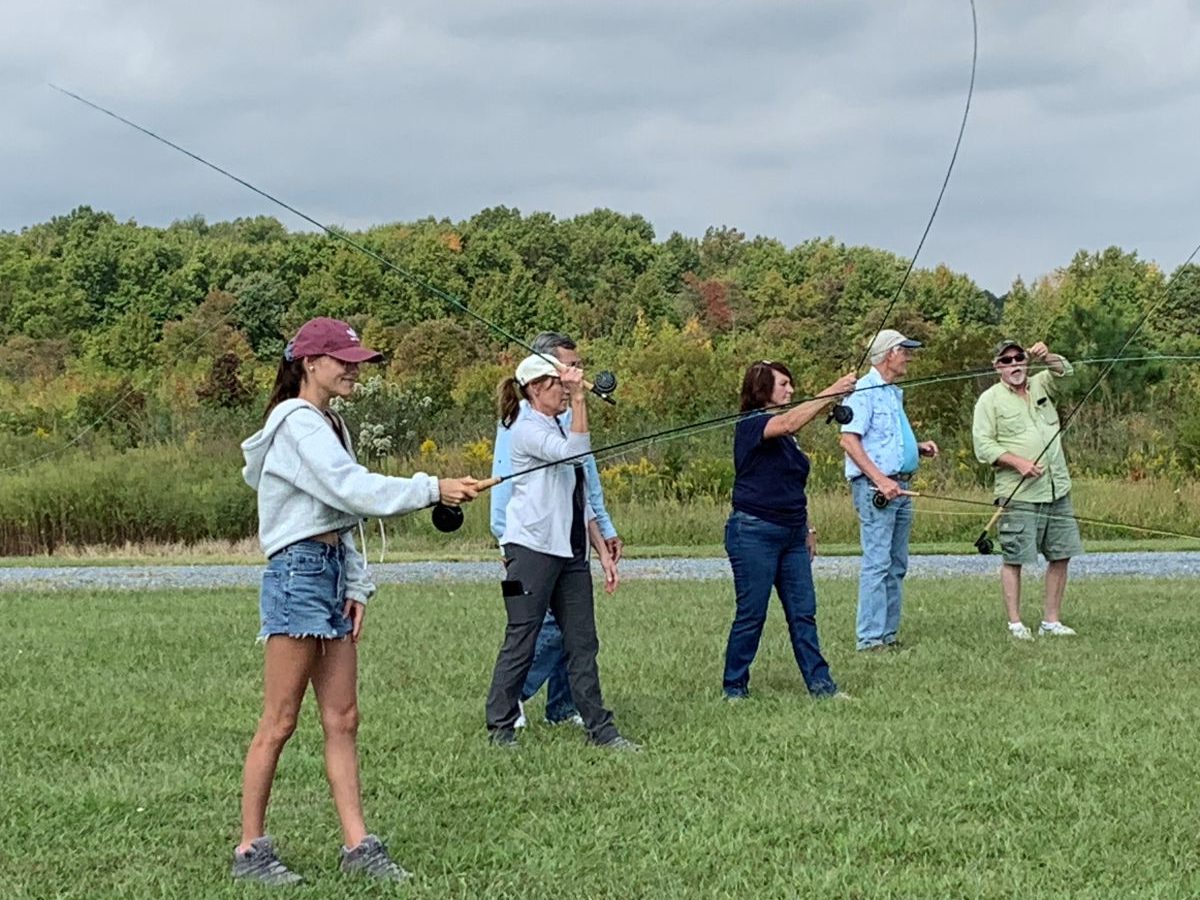 A group of adults stand in a field practicing fly-casting technique.