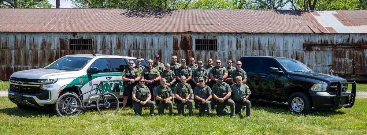 A group of DNREC Natural Resources Police Officers pose with two police vehicles and a bicycle.