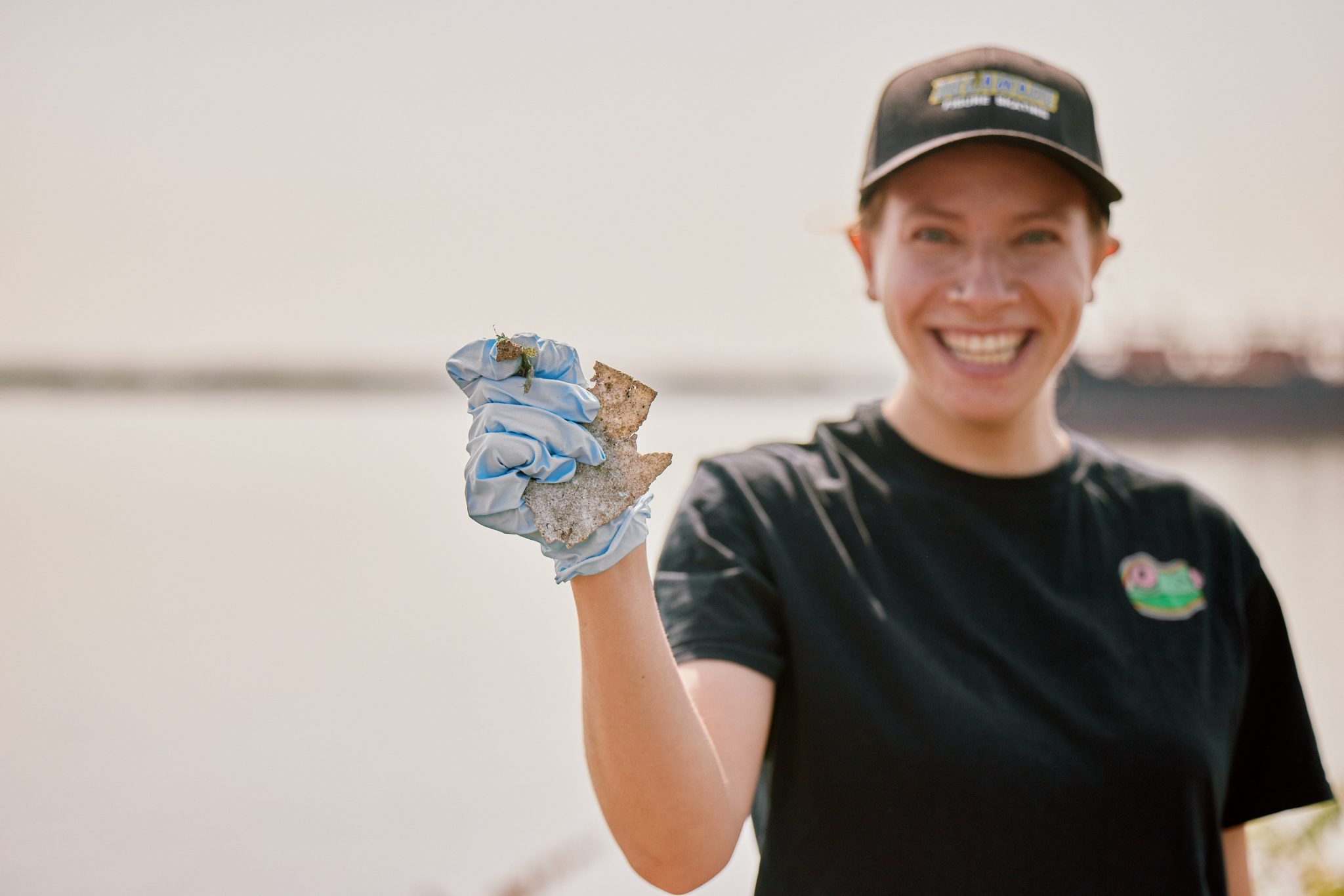 Volunteer at a previous Coastal Cleanup smiling and holding up trash collected off of the beach.