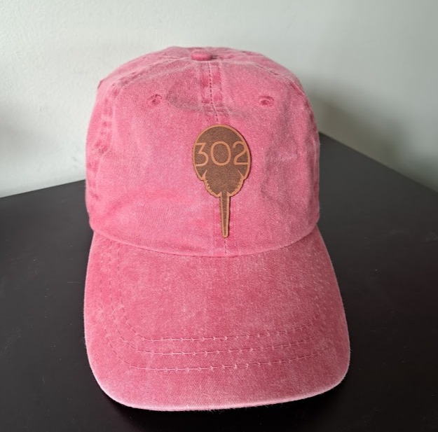 A pink hat has a horseshoe crab image on it with 302 in the center.