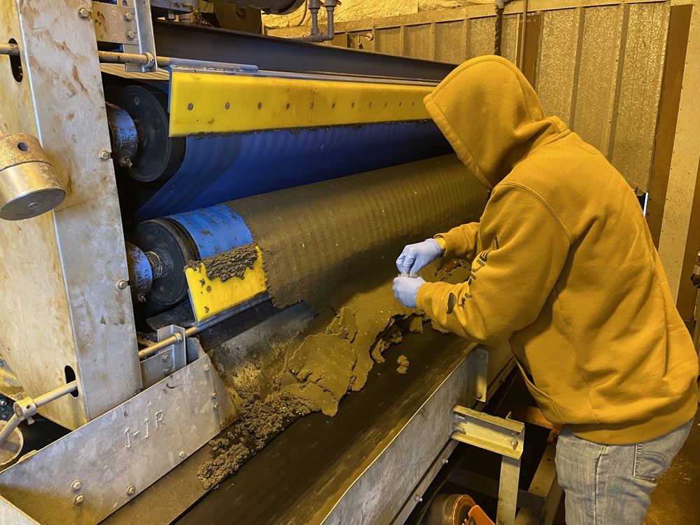 A person takes a sample of biosolids.