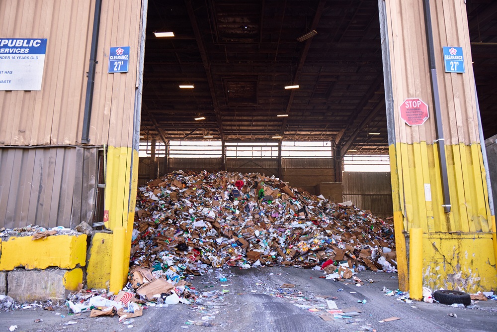 A large pile of recyclables, including plastic and paper, sits in a warehouse.