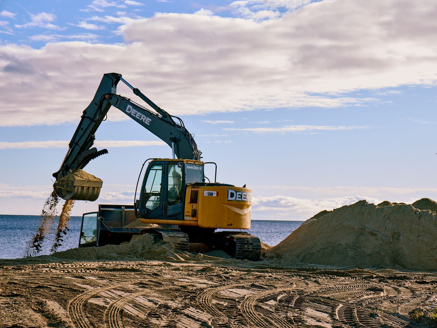 A large yellow construction vehicle with a scoop moving sand on a beach.