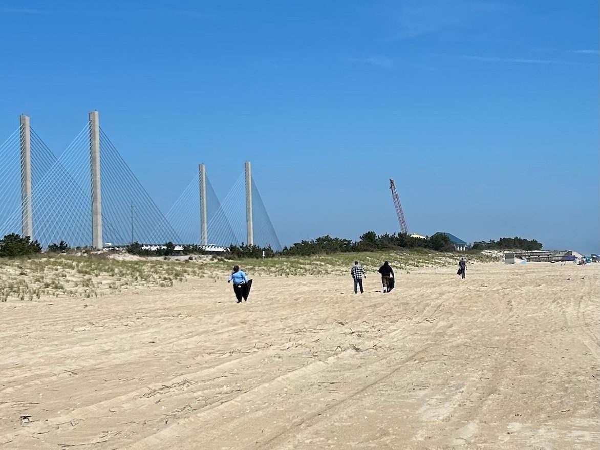 People walk down a beach carrying trash bags.