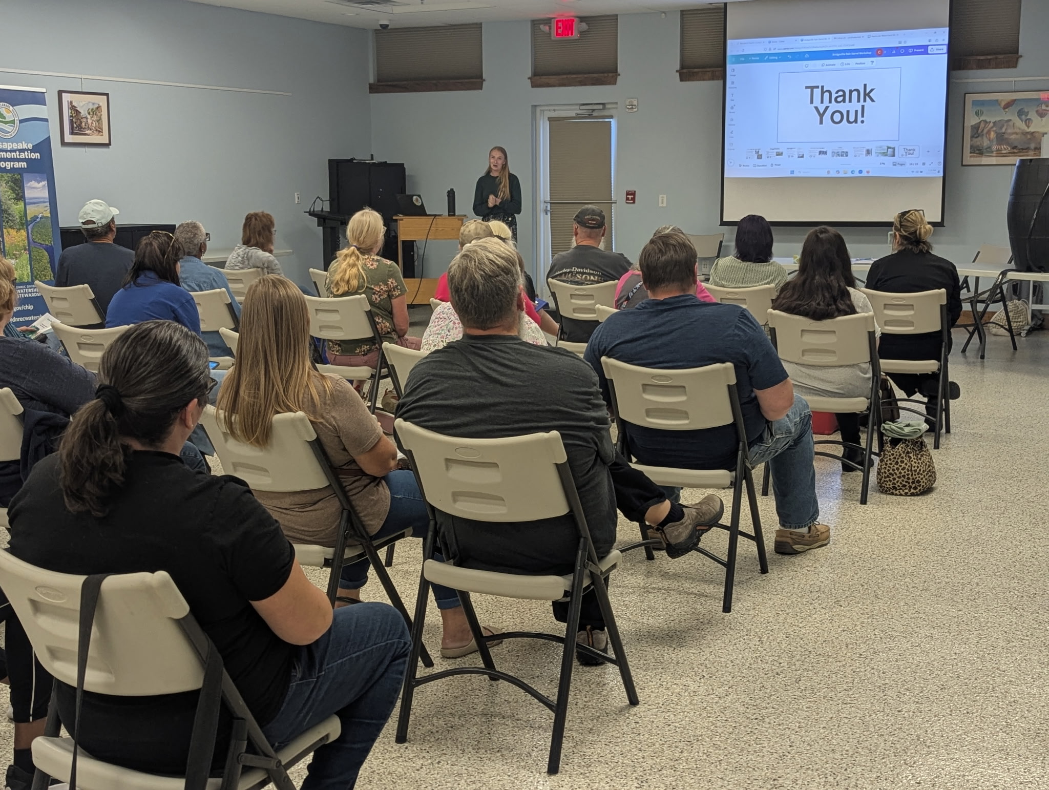 Workshop attendees, seated, seen from behind, face a screen and a presenter.