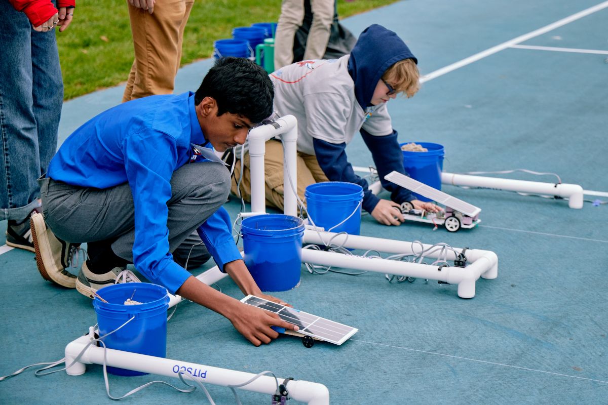 Two students crouch at the starting line, preparing their solar-powered model cars for a race.