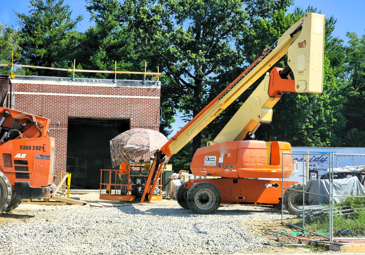 Construction vehicles working around a brick building under construction.