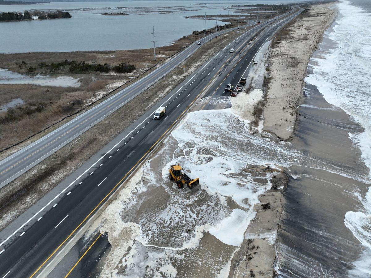 Heavy equipment pushes sand off of two lanes of a highway that have been closed by the ocean washing over coastal dunes and partially flooding the road.
