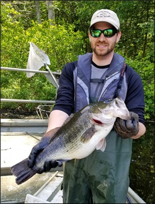 A man in waders holds up a large freshwater fish.