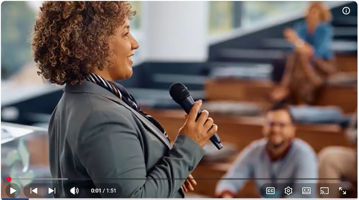 A confident woman holding a microphone speaks to an attentive audience. 