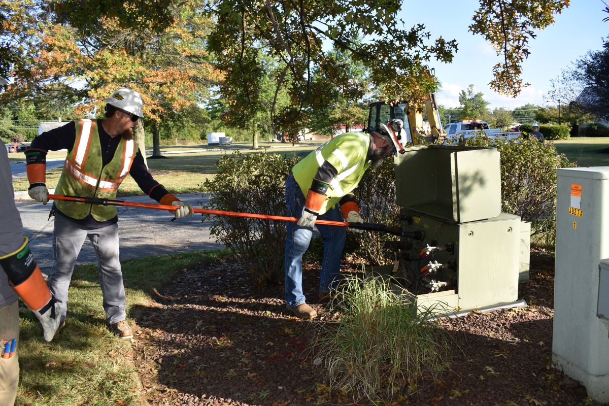 Two utility works perform maintenance on an electrical junction box.