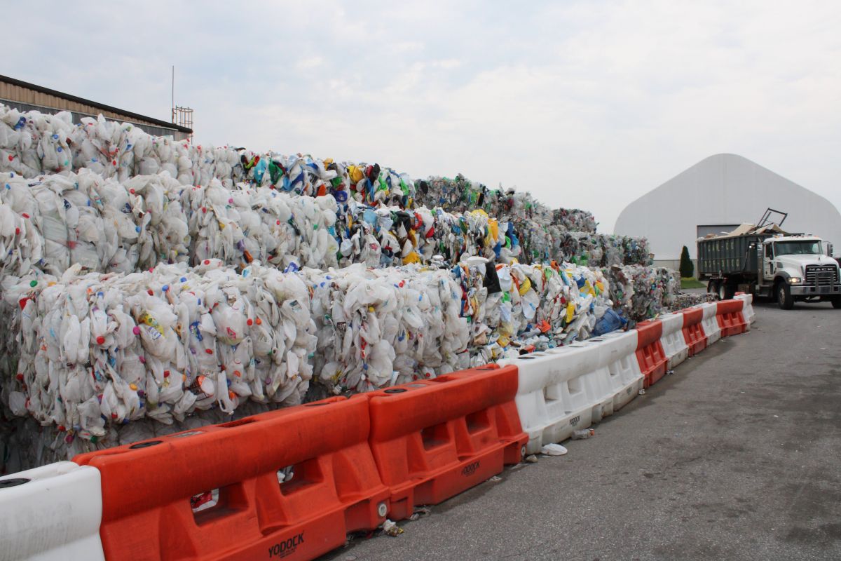 Large bales of recyclable materials stacked four-high at a material management center with a truck in the background.